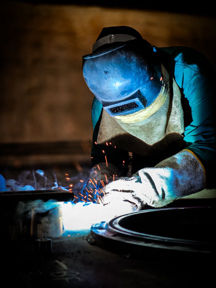 Intrepid Metal Works | Custom Fencing & Fabrication Las Vegas Close-up of a welder working with sparks in a dimly lit workshop.