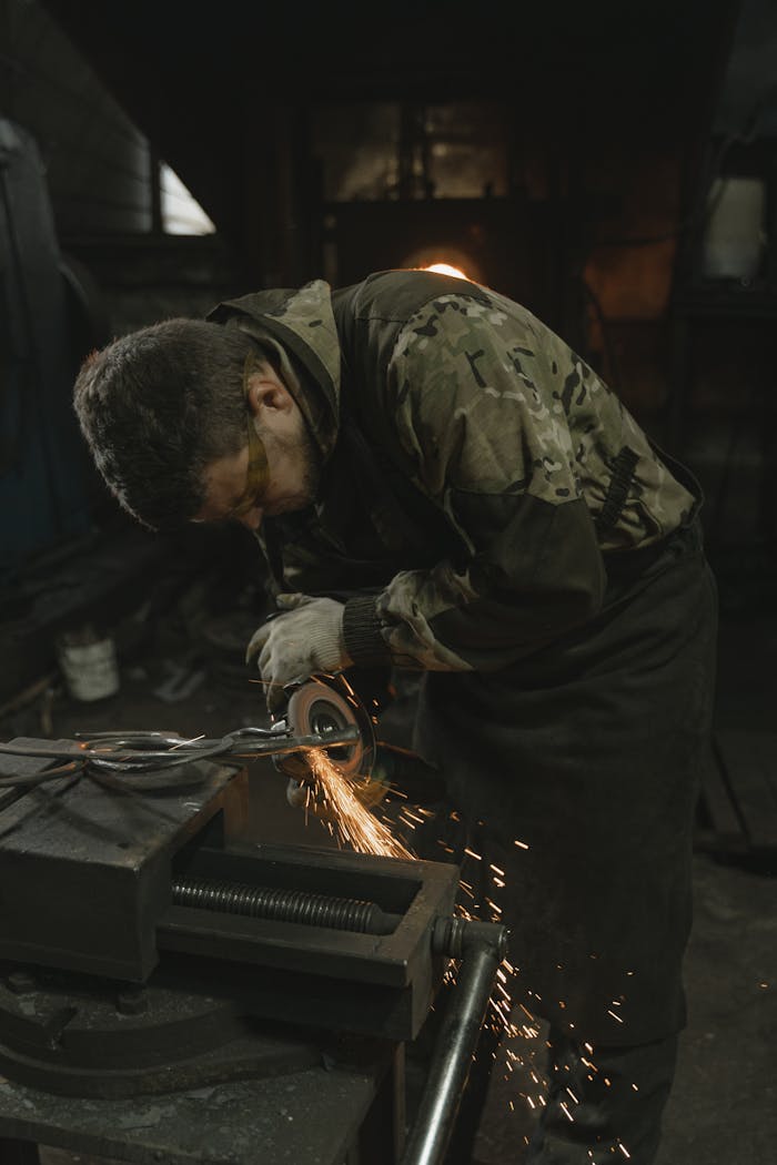 Intrepid Metal Works | Custom Fencing & Fabrication Las Vegas A blacksmith skillfully grinds metal, creating sparks in a workshop.